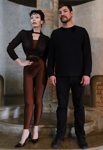 Full-figure portrait of Corin Ism and Markus Amalthea Magnuson in an old stone and brick church interior